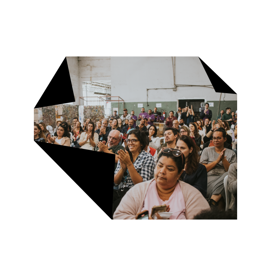 Pessoas aplaudindo uma palestra em uma cooperativa de reciclagem.